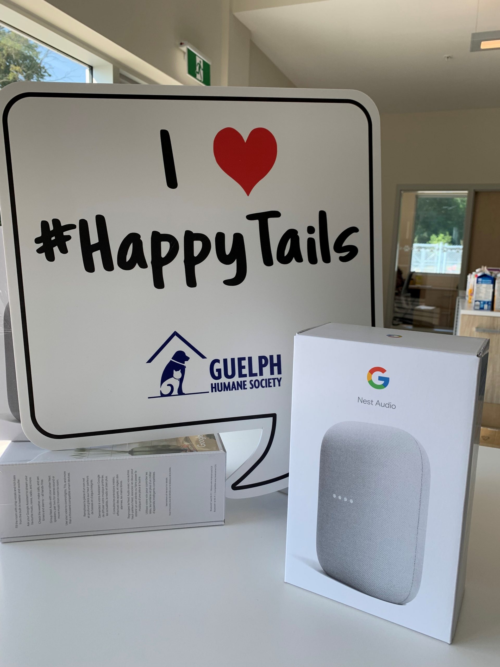 Google Nest speaker box beside a sign that reads "I love #HappyTails" with the Guelph Humane Society logo