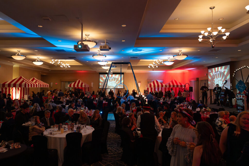 Guests seated at round tables in a ballroom with colourful stage lighting at the Happy Tails Gala