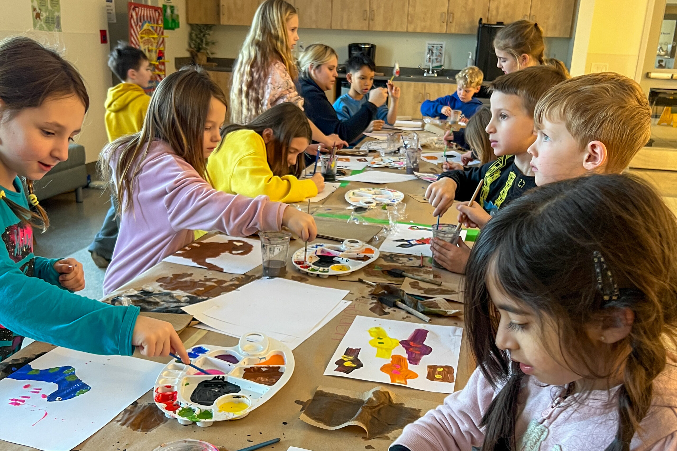 Children painting at a long table during a craft activity